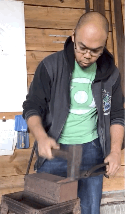 GIF of young man in a harry potter jacket hammering a piece of metal on a block.