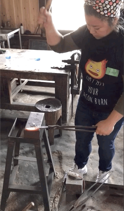 GIF of young woman hammering a piece of hot metal on a block.