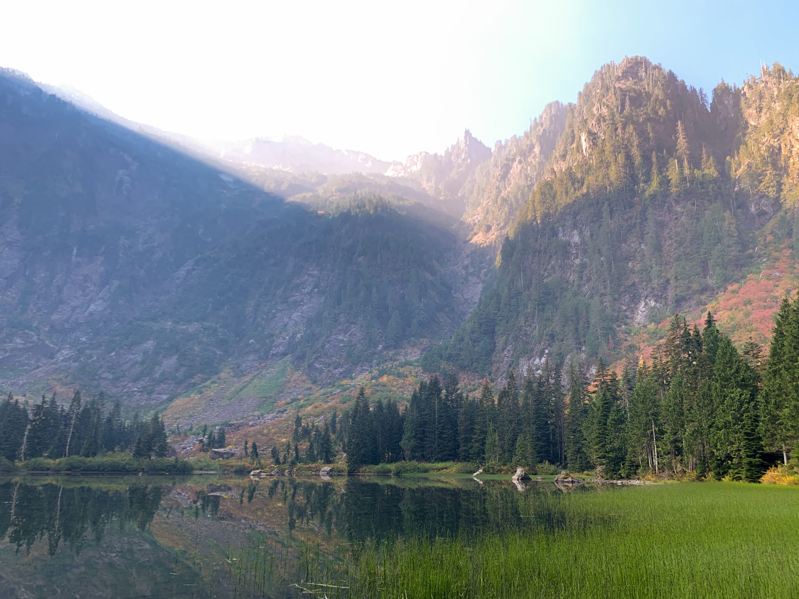 Beautiful view of Heather Lake in the Snoqualmie National Forest surrounded by lush green trees with sunlight peaking over the mountain tops.